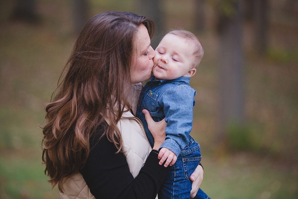A lifestyle portrait of everyday motherhood when a mom kisses her baby boy during a family session in the Boston Arboretum
