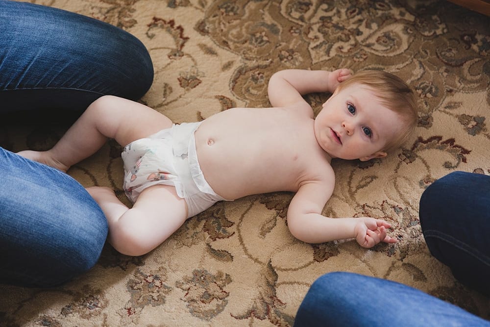 A lifestyle photograph of a baby boy laying on the floor in his diaper before he gets dress during a family session at home in Boston, Massachusetts