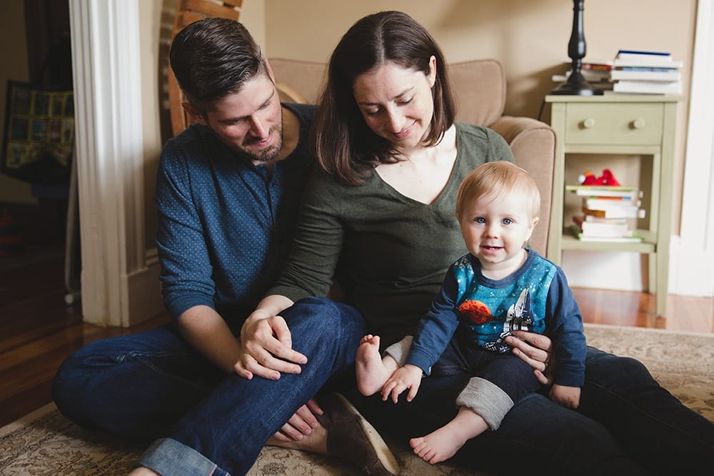 A lifestyle photograph a mother and father sitting on the floor with their baby boy during a family session at home in Boston, Massachusetts