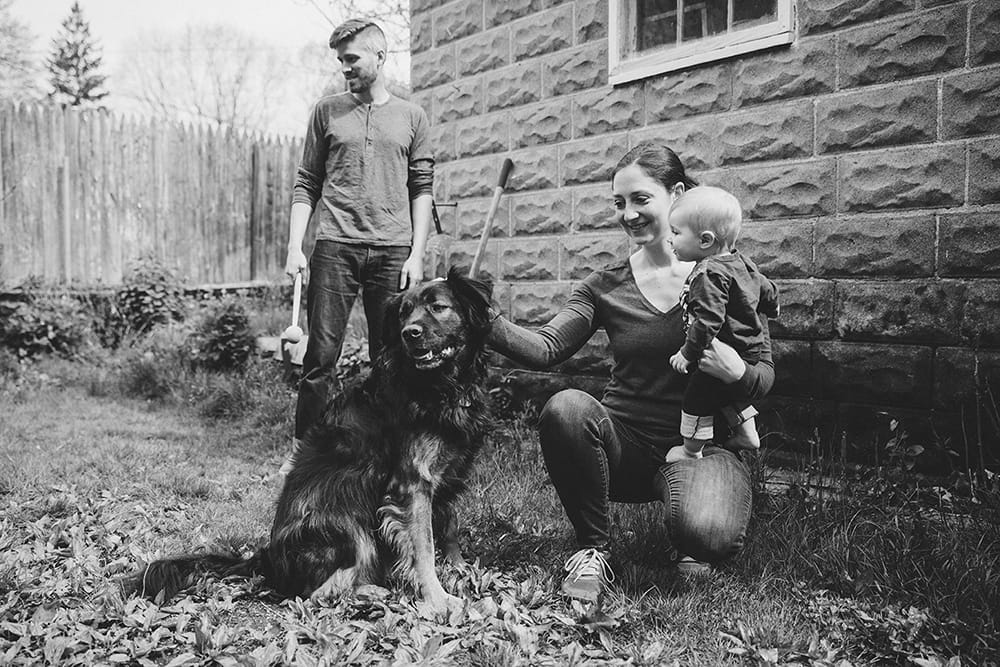 A documentary photograph of a mother holding her baby boy and petting their dog during a family session at home in Boston, Massachusetts