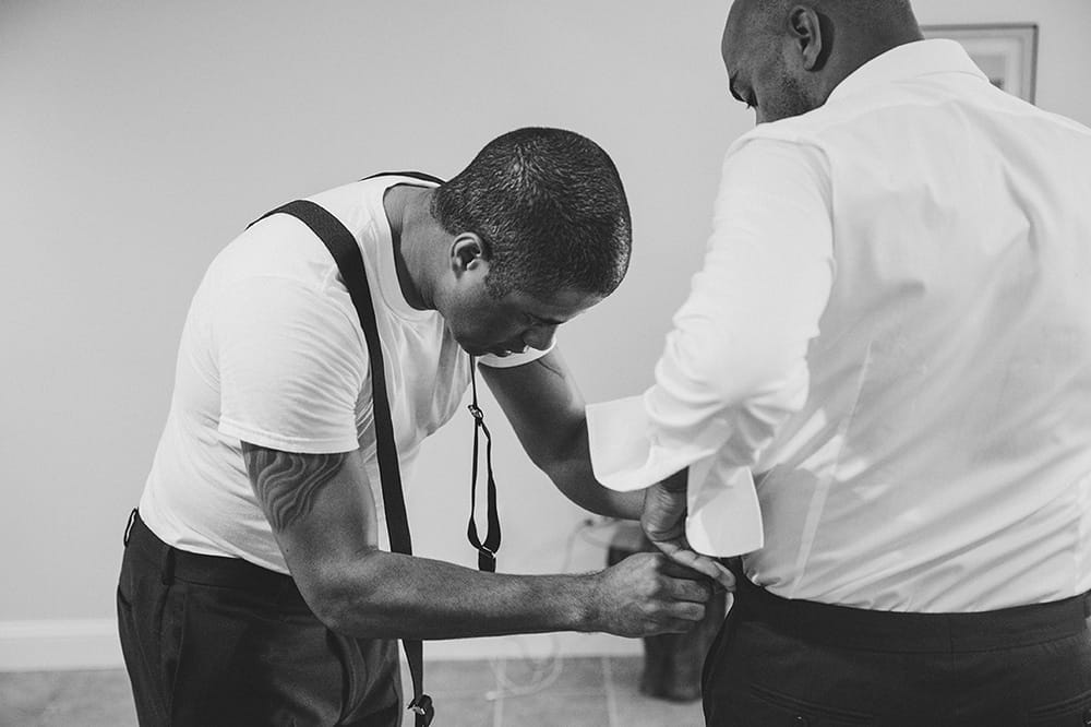 A documentary photograph of a Groomsmen helping the Groom with his suspenders before a Martha's Vineyard wedding