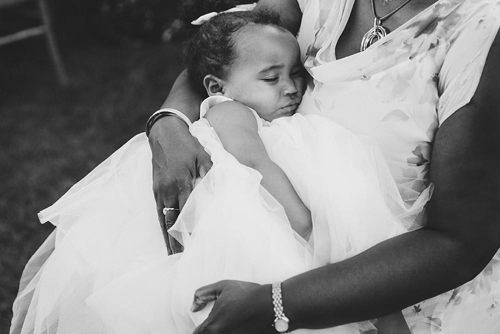 A documentary photograph of a flower girl sleeping on her grandma's lap during a Martha's Vineyard Wedding