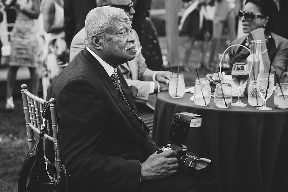 A documentary photograph of a guest sitting with a camera at the cocktail hour of a Martha's Vineyard Wedding