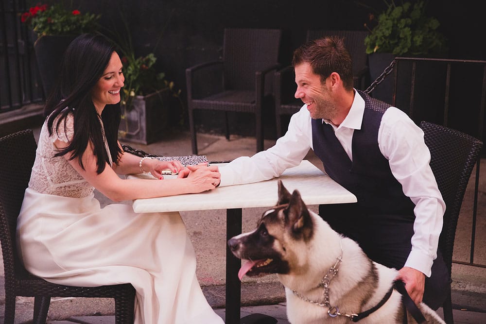A documentary photograph of a couple sitting outside Marliave Restaurant with their dog during a Boston Engagement Session