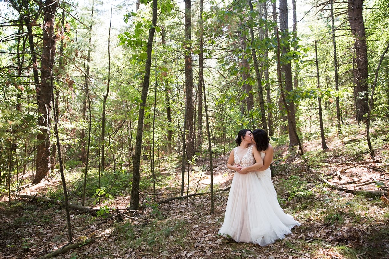 A natural and romantic photograph of two bride kissing in the woods during the first look at their Friendly Crossways Wedding