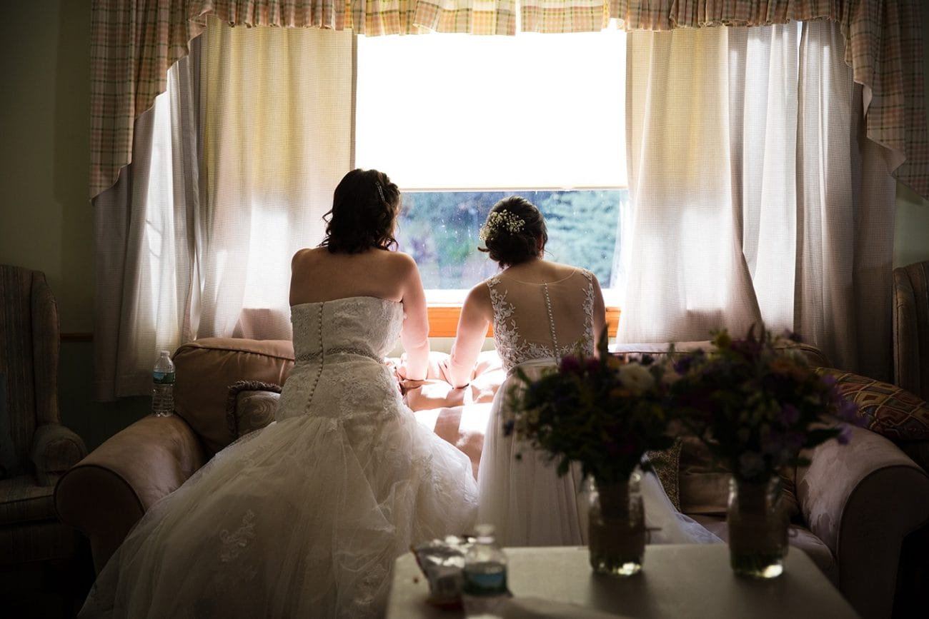 A documentary photograph of two brides watching their guest arrive from a window before their Friendly Crossways Wedding