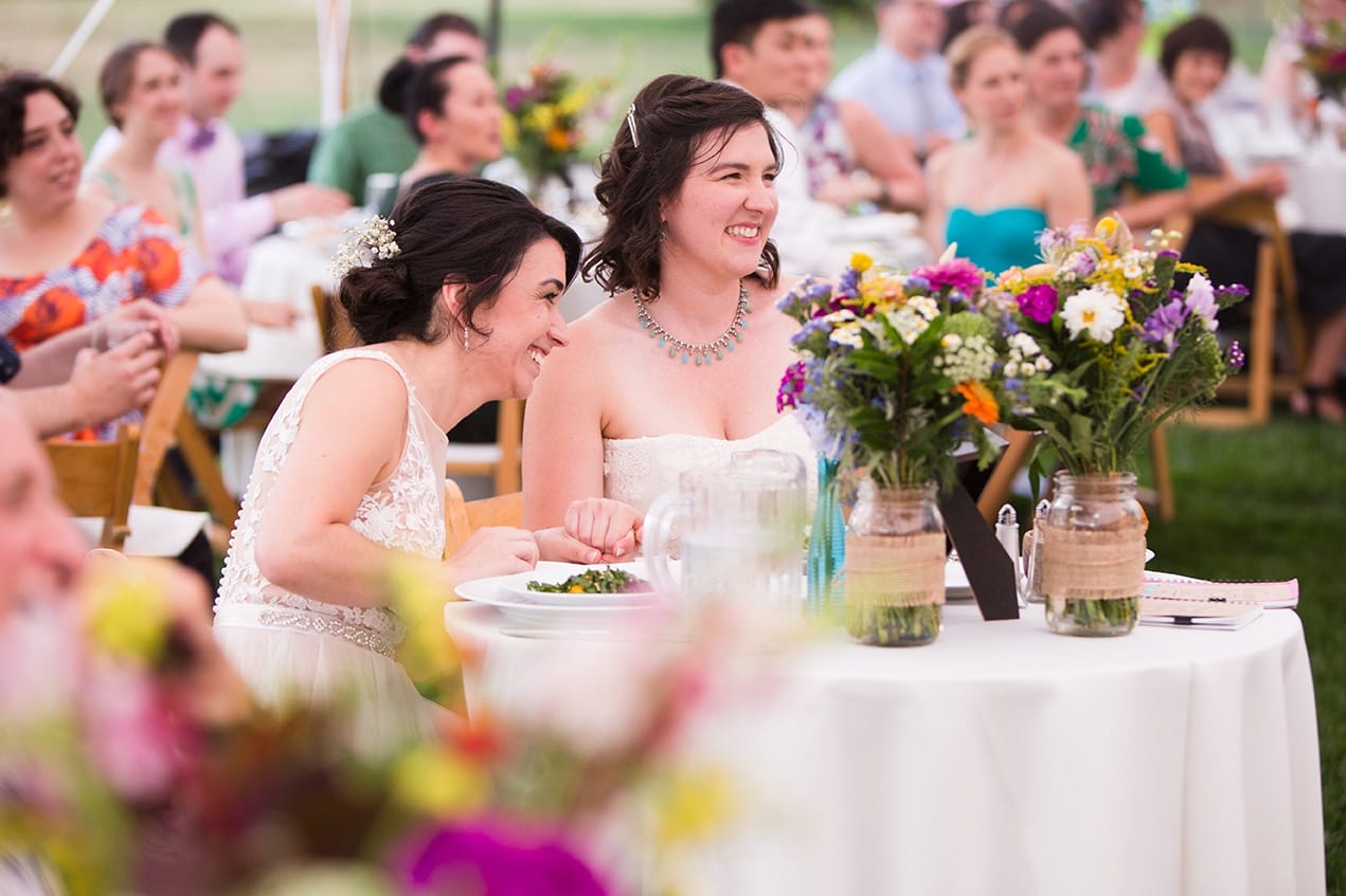 A documentary photograph of two brides laughing during the toasts at their Friendly Crossways Wedding