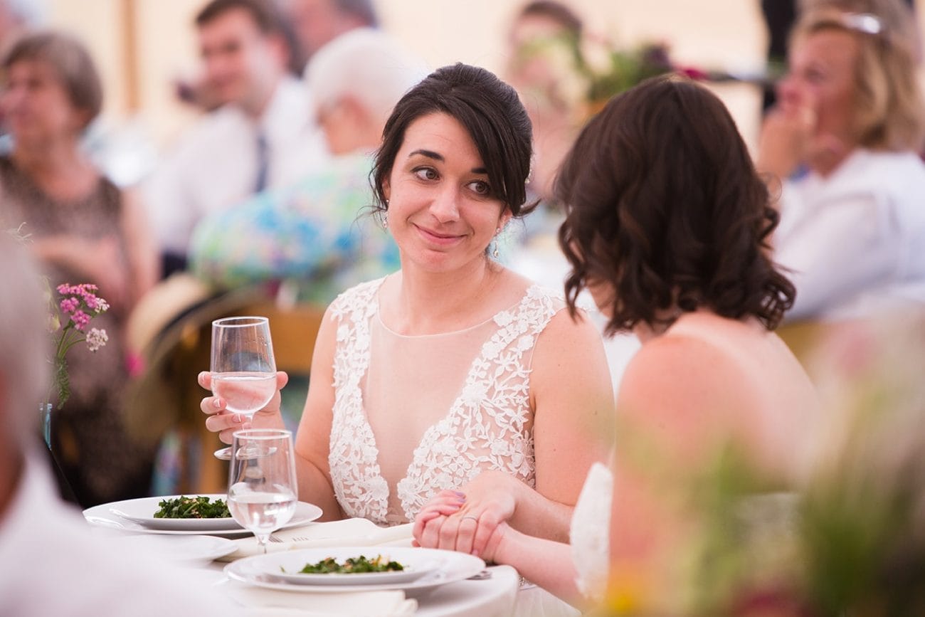 A documentary photograph of two brides looking at each other during the toasts at their Friendly Crossways Wedding