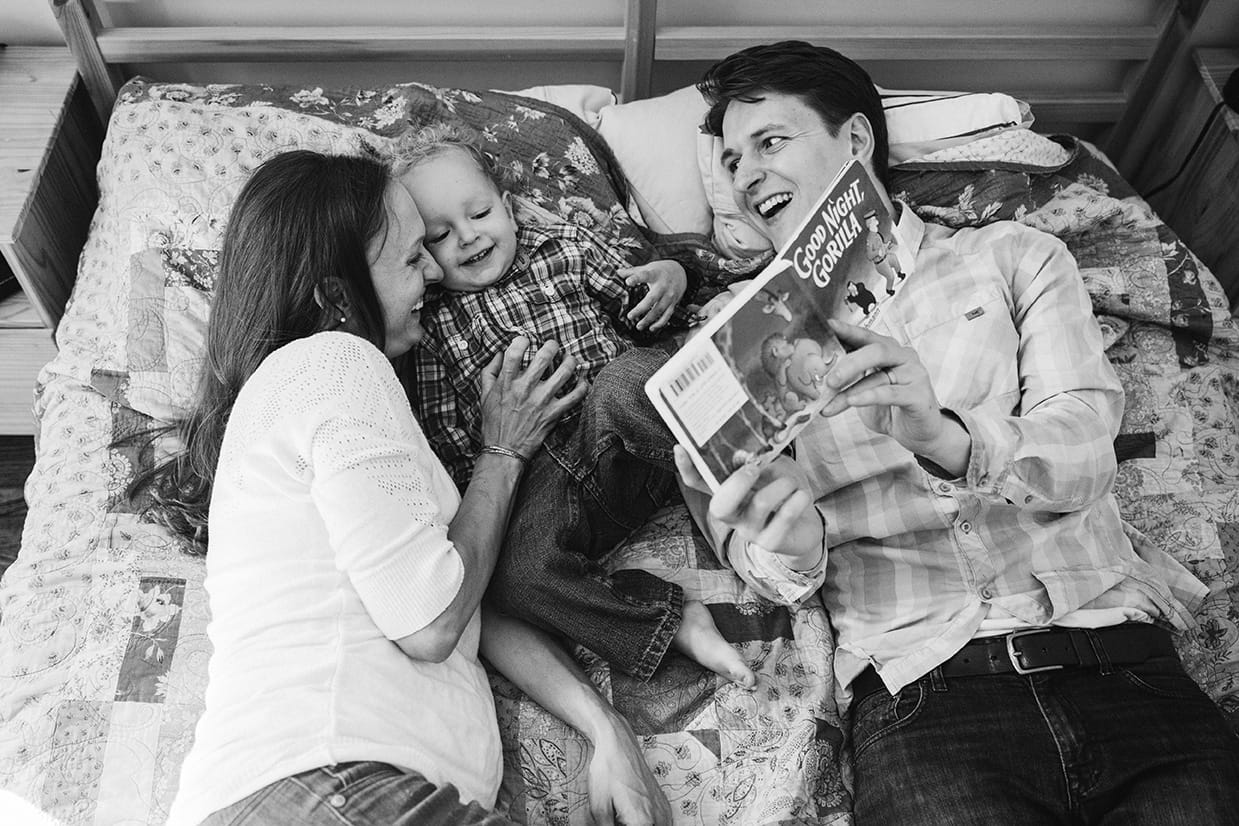 A family read books together in bed during their in home family session in Boston