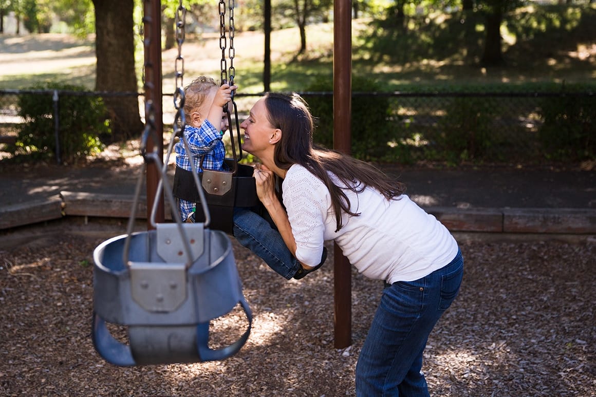 A documentary photograph of a mother pushing her son on the swings during an in home family session in Boston
