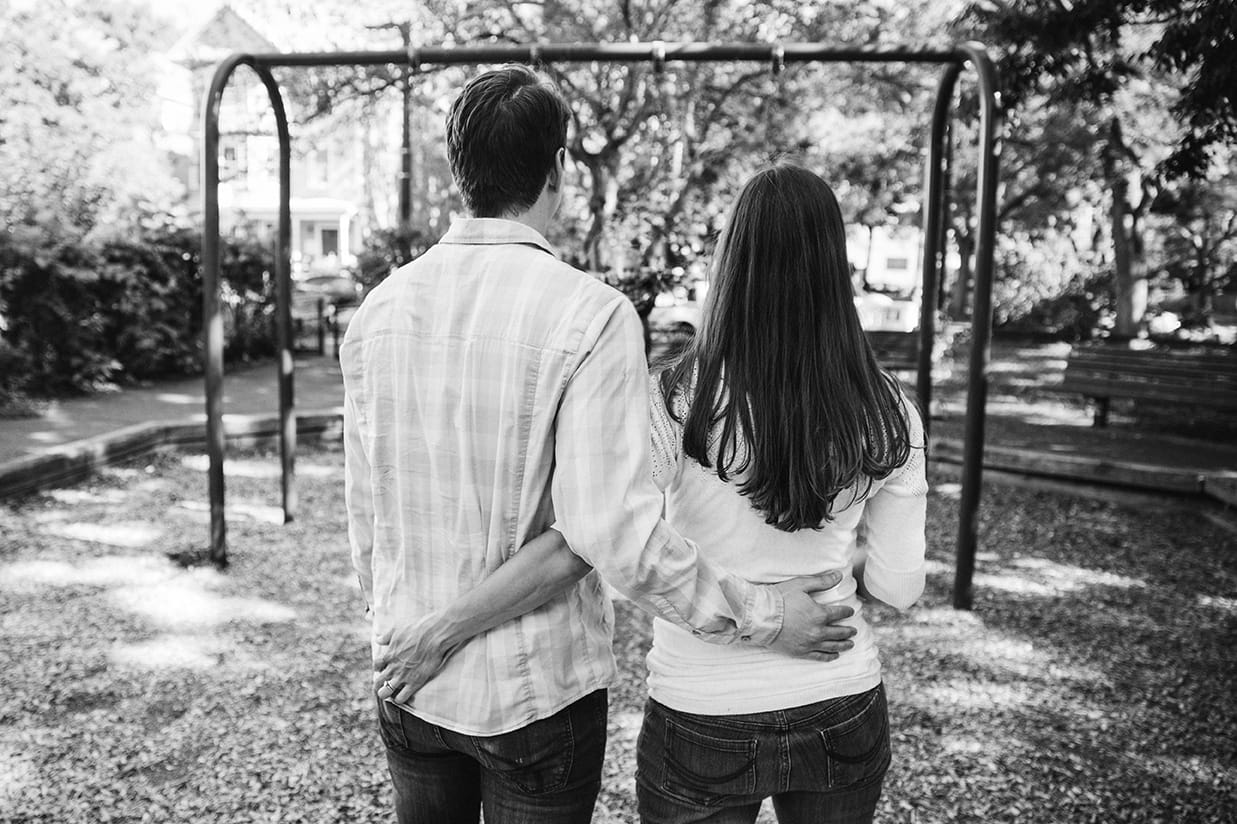 A lifestyle photograph of a mom and dad watching their son on the swings during their in home family session in Boston