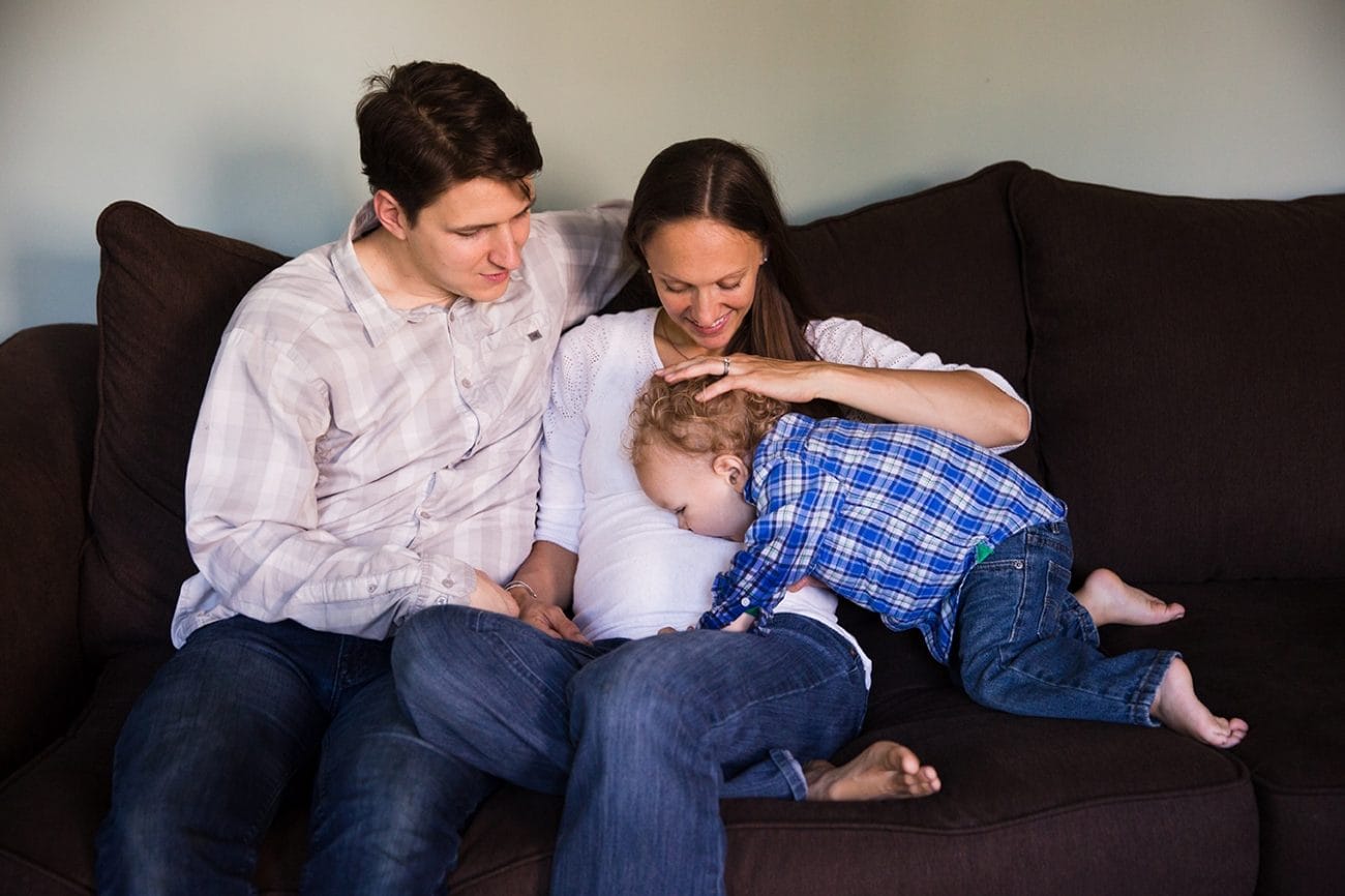 A lifestyle photograph of a boy kissing his mother's baby bump during an in home family session in Boston
