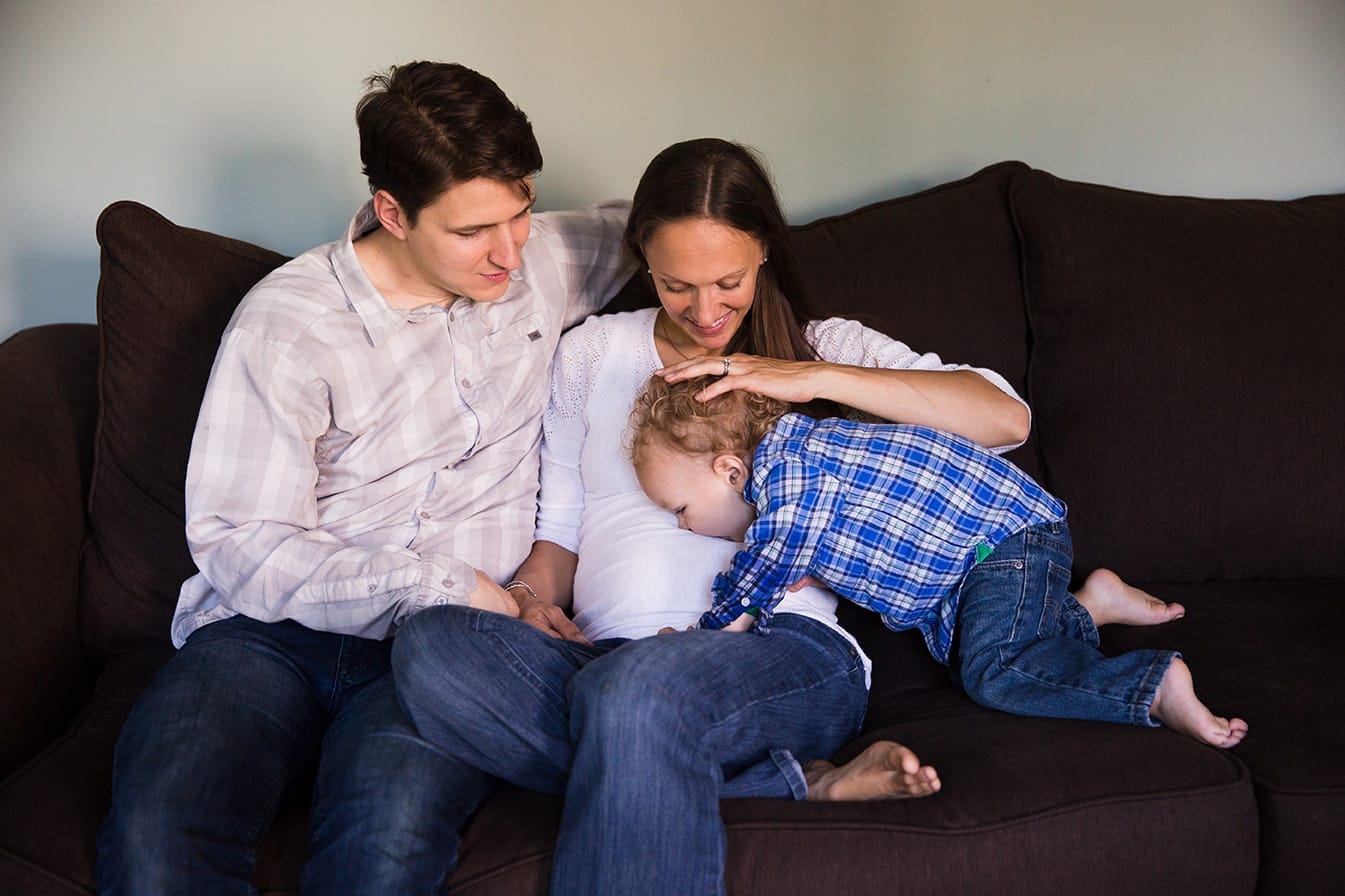 A lifestyle photograph of a boy kissing his mother's baby bump during an in home family session in Boston