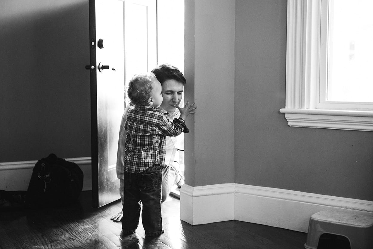 A documentary photograph of a boy kissing his Dad goodbye during an in home family session in Boston