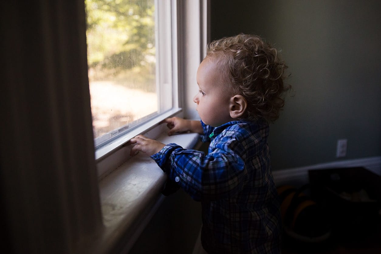 A documentary photograph of boy looking out the window during their in home family session in Boston