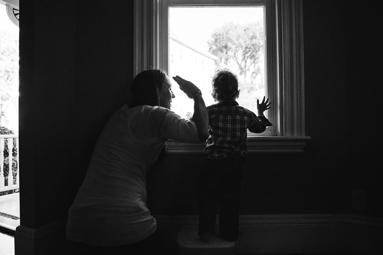 A documentary photograph of mother and son waving goodbye to Dad during an in home family session in Boston