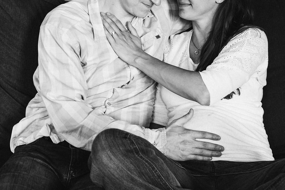 A lifestyle photograph of an expecting couple cuddling on the couch during their in home family session in Boston