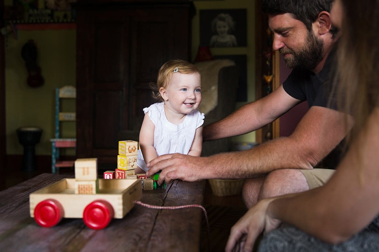 A documentary photograph of a toddler stacking blocks with her parents during an evergreen family session at their Colorado home