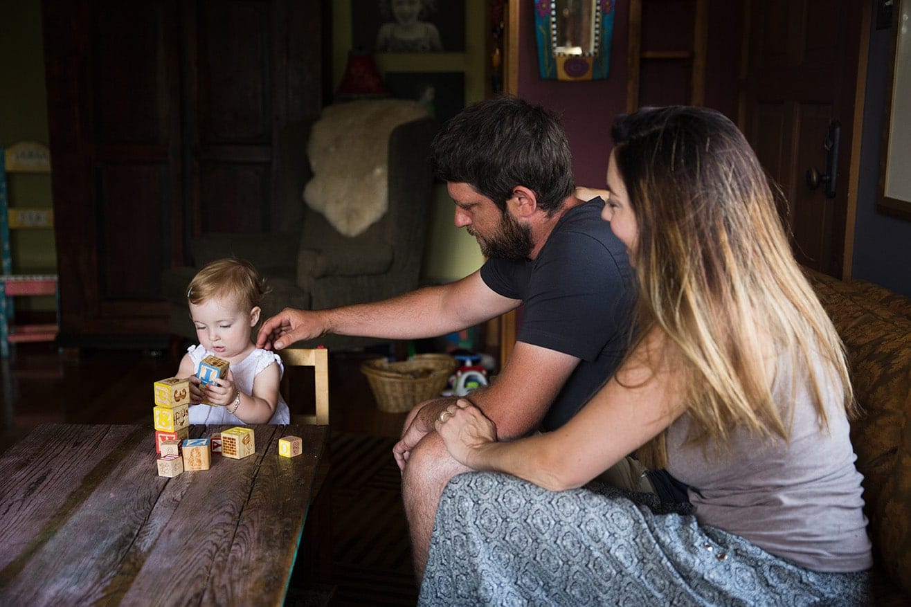 A documentary photograph of a toddler stacking blocks with her parents during their evergreen family session at home in Colorado