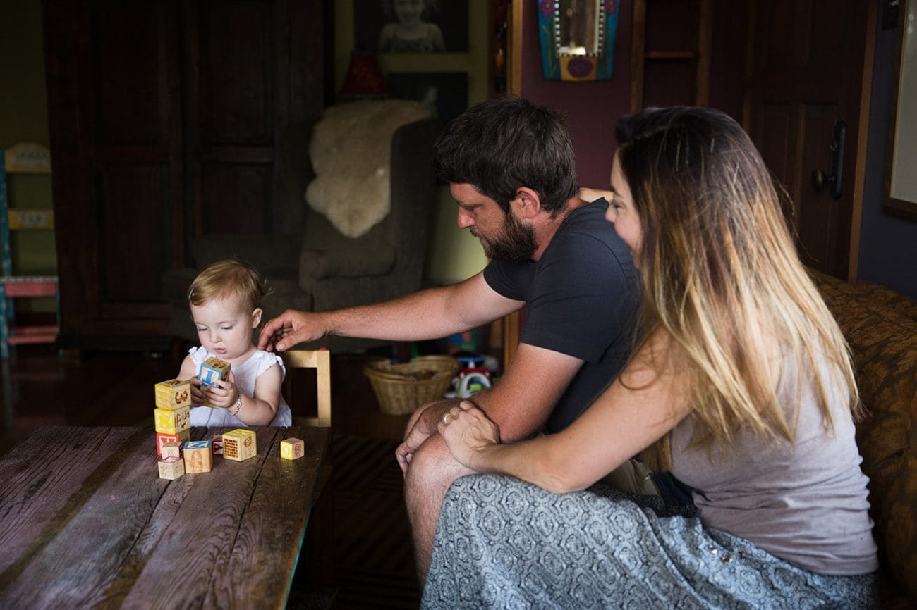 A documentary photograph of a toddler stacking blocks with her parents during their evergreen family session at home in Colorado