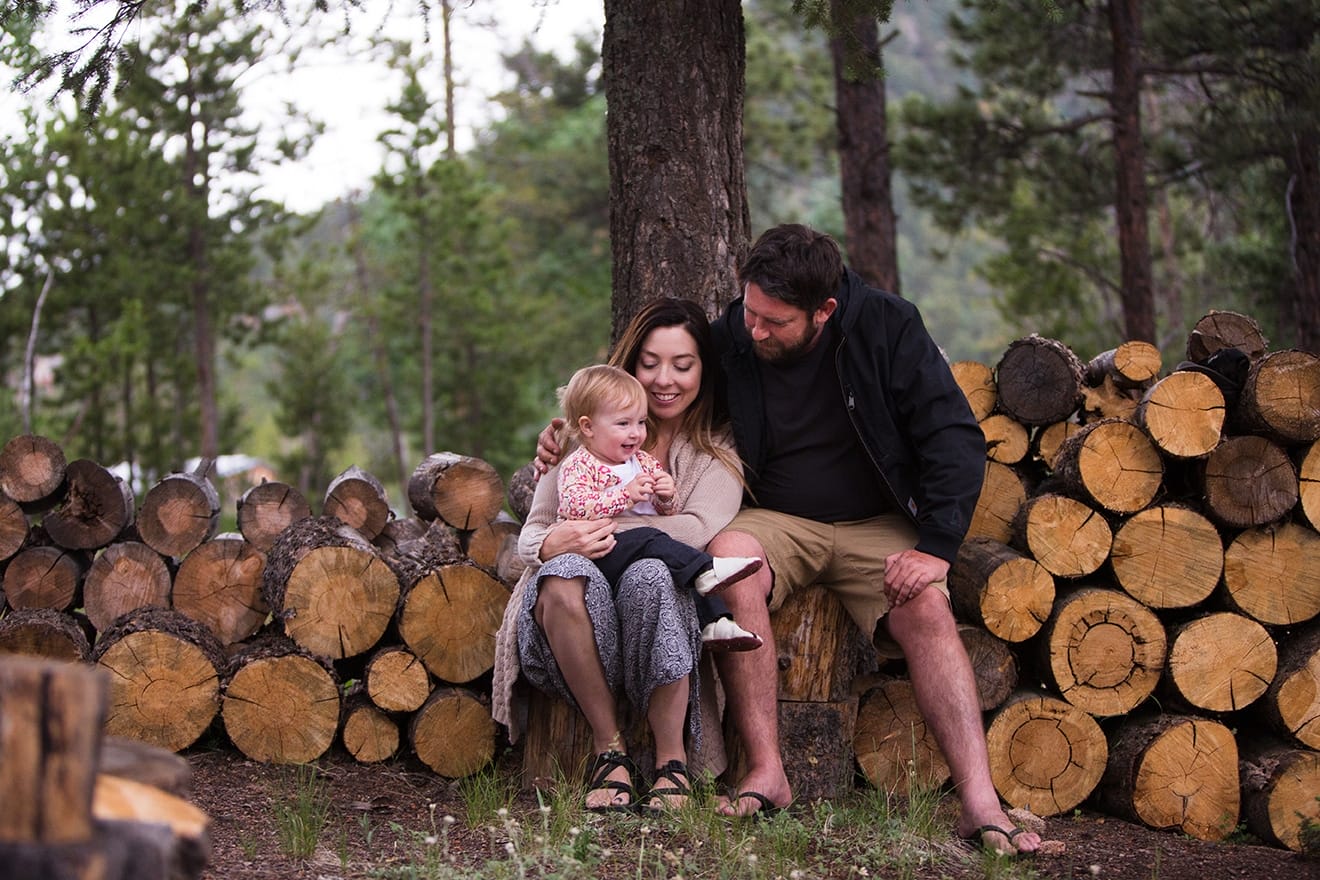 A lifestyle photograph of a family sitting on a wood pile during their evergreen family session at home in Colorado