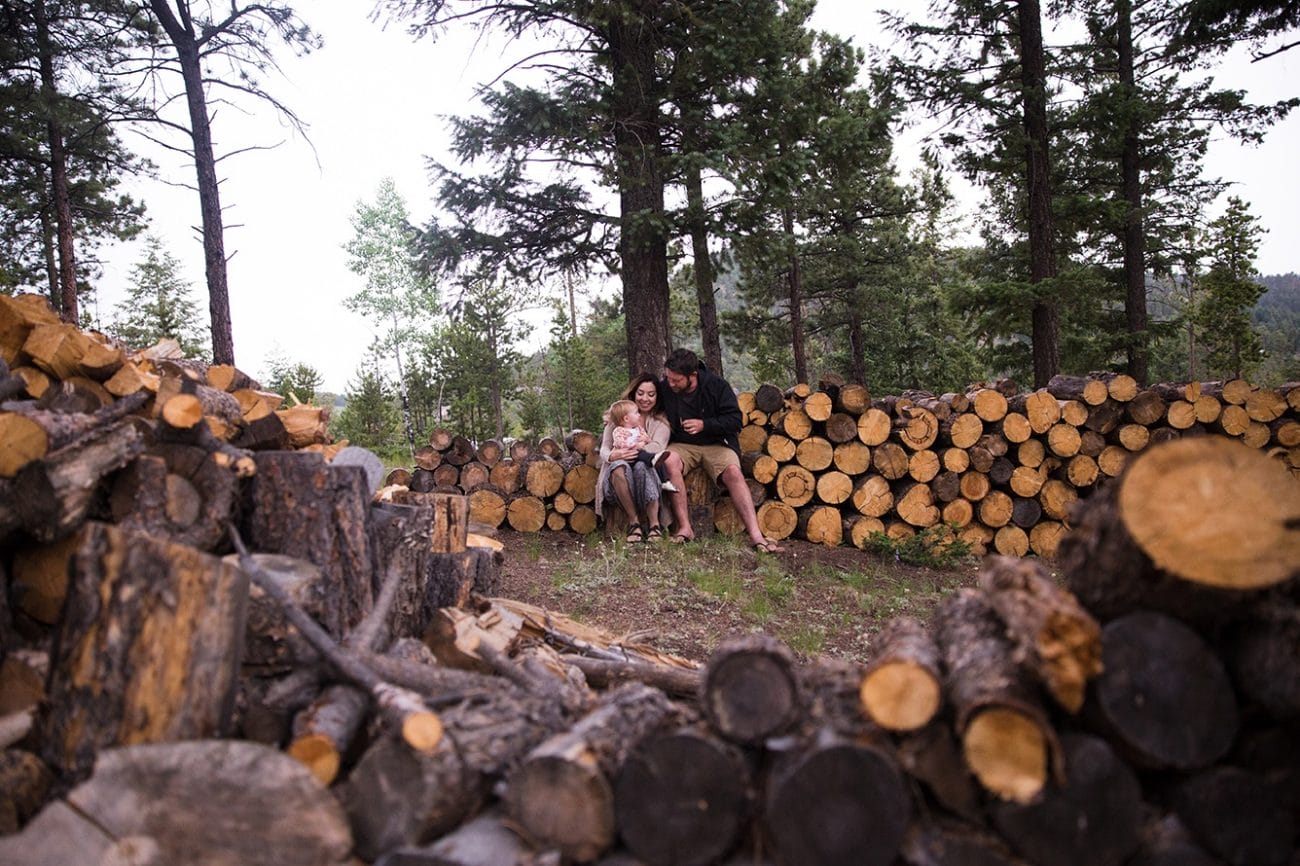 A lifestyle photograph of a family sitting on a wood pile during their evergreen family session at home in Colorado