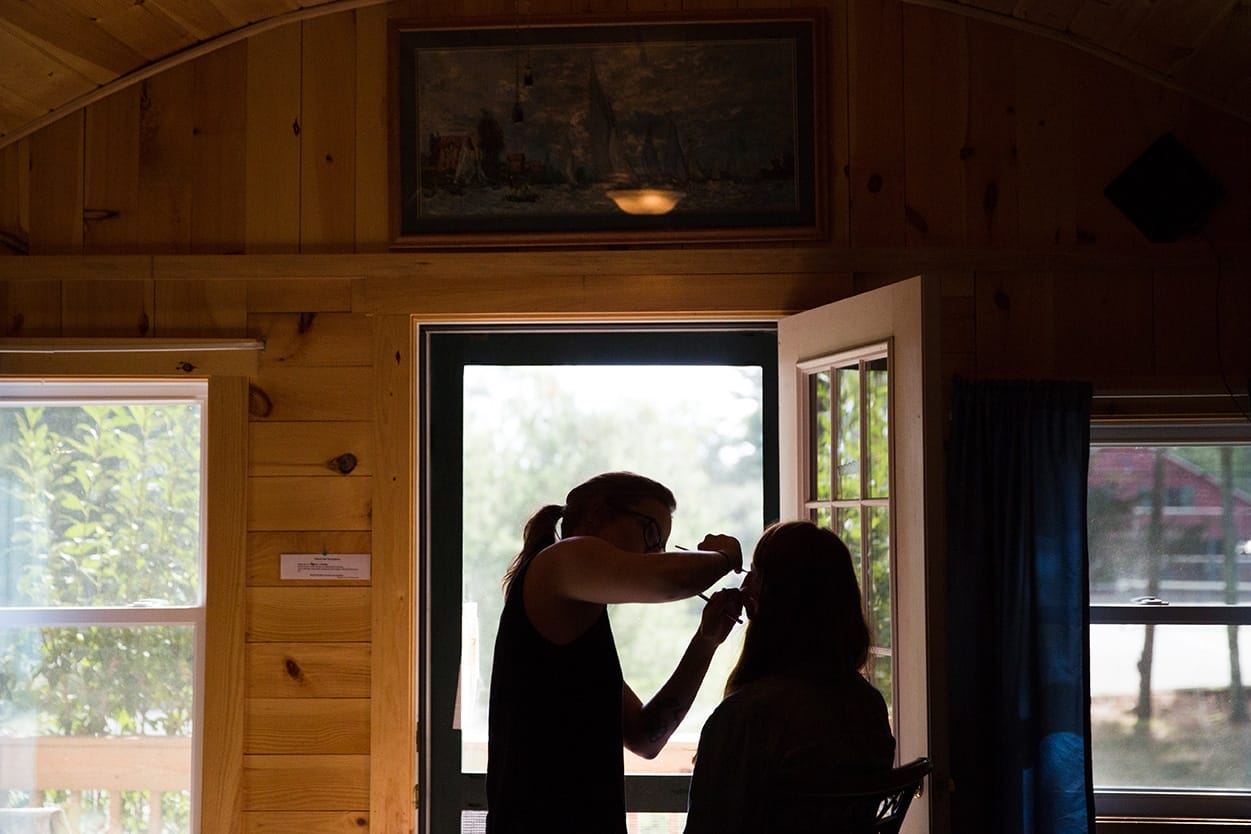 A documentary photograph of a bride getting her makeup done before her Kingsley Pines Camp Wedding in Maine