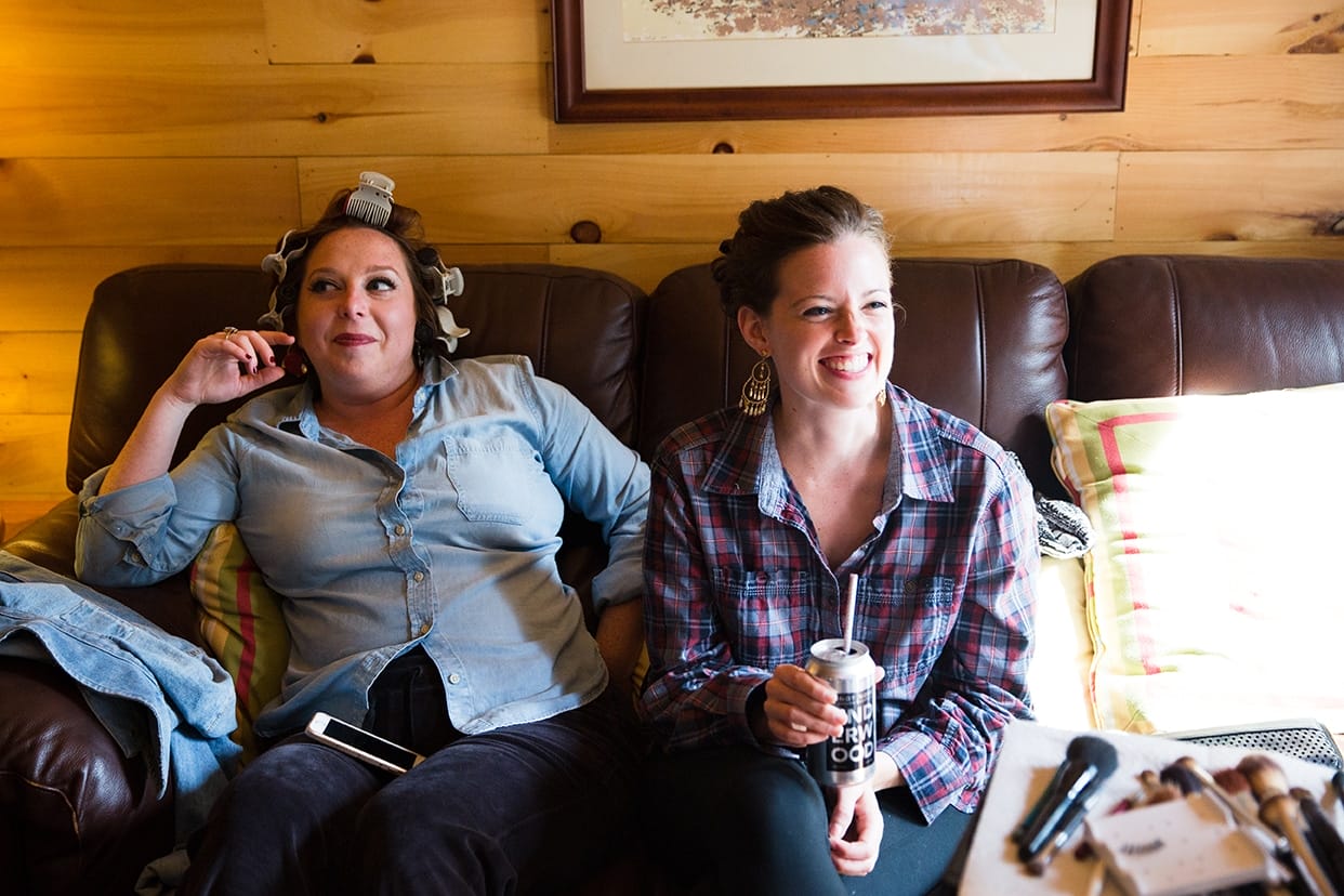 A documentary photograph of bridesmaids laughing while they get ready for a Kingsley Pines Camp Wedding in Maine