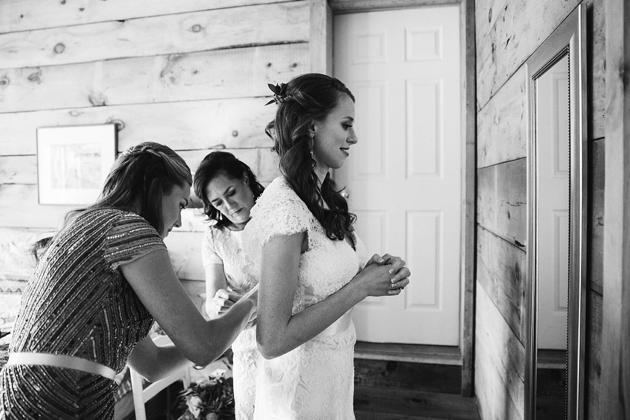 A documentary photograph of a bride putting her dress on before her Kingsley Pines Camp Wedding in Maine