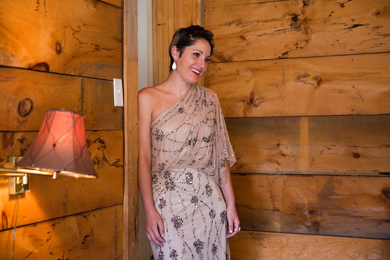 A documentary photograph of a bridesmaid watching the bride put her dress on before her Kingsley Pines Camp Wedding in Maine