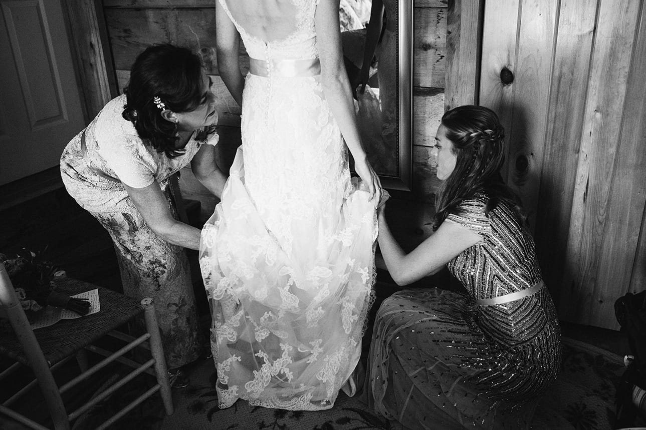 A documentary photograph of a bride putting her dress on before her Kingsley Pines Camp Wedding in Maine