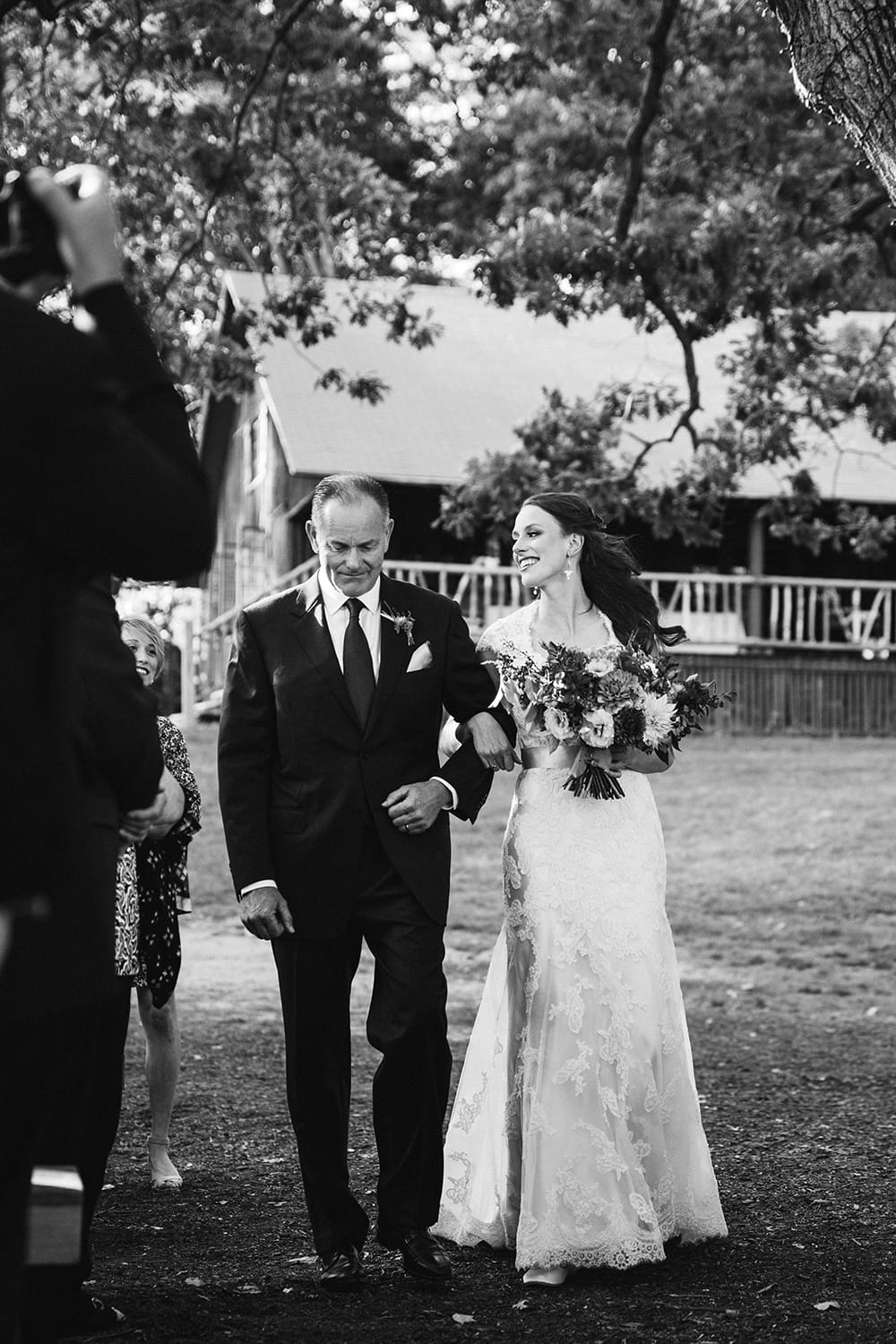 A documentary photograph of a bride and her father walking down the aisle during her Kingsley Pines Camp Wedding in Maine
