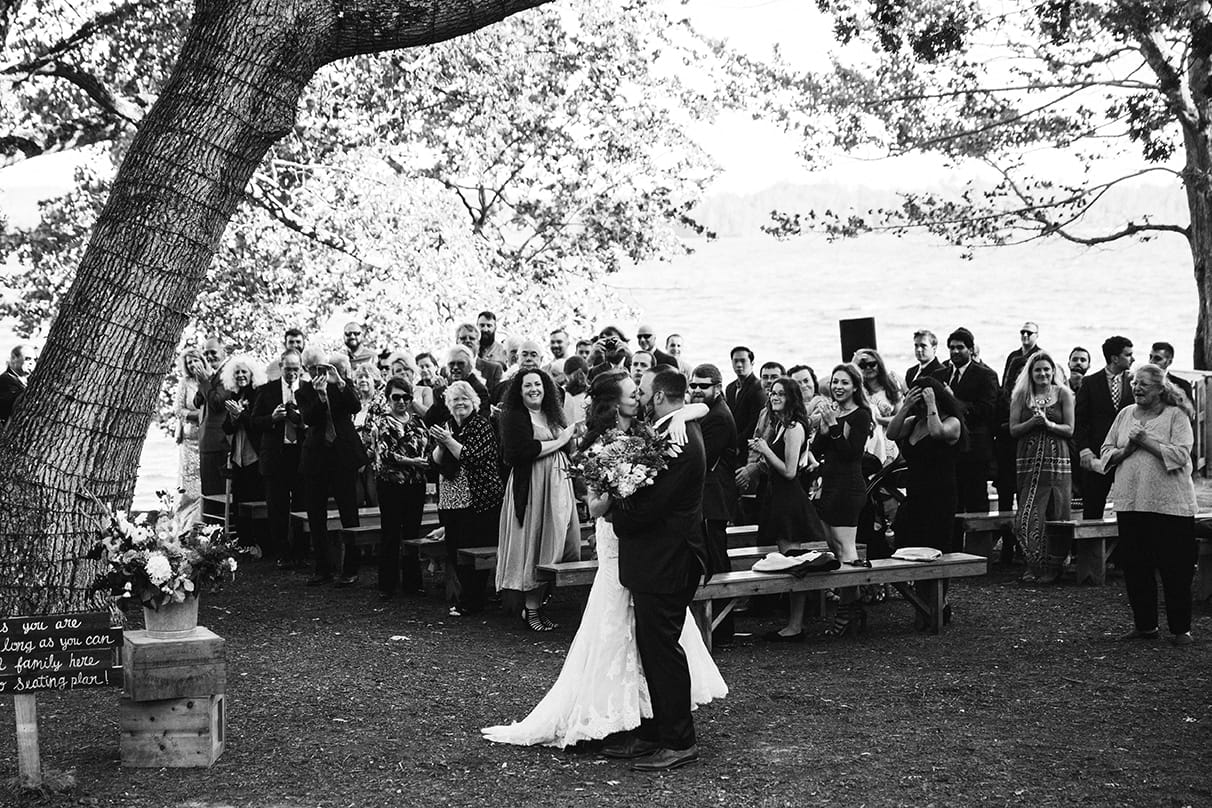 A documentary photograph of a bride and groom kissing after their outdoor wedding ceremony at Kingsley Pines Camp in Maine