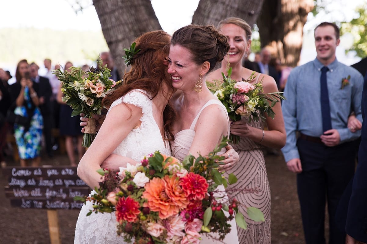 A documentary photograph of bride hugging her bridesmaid after her outdoor wedding ceremony at Kingsley Pines Camp in Maine
