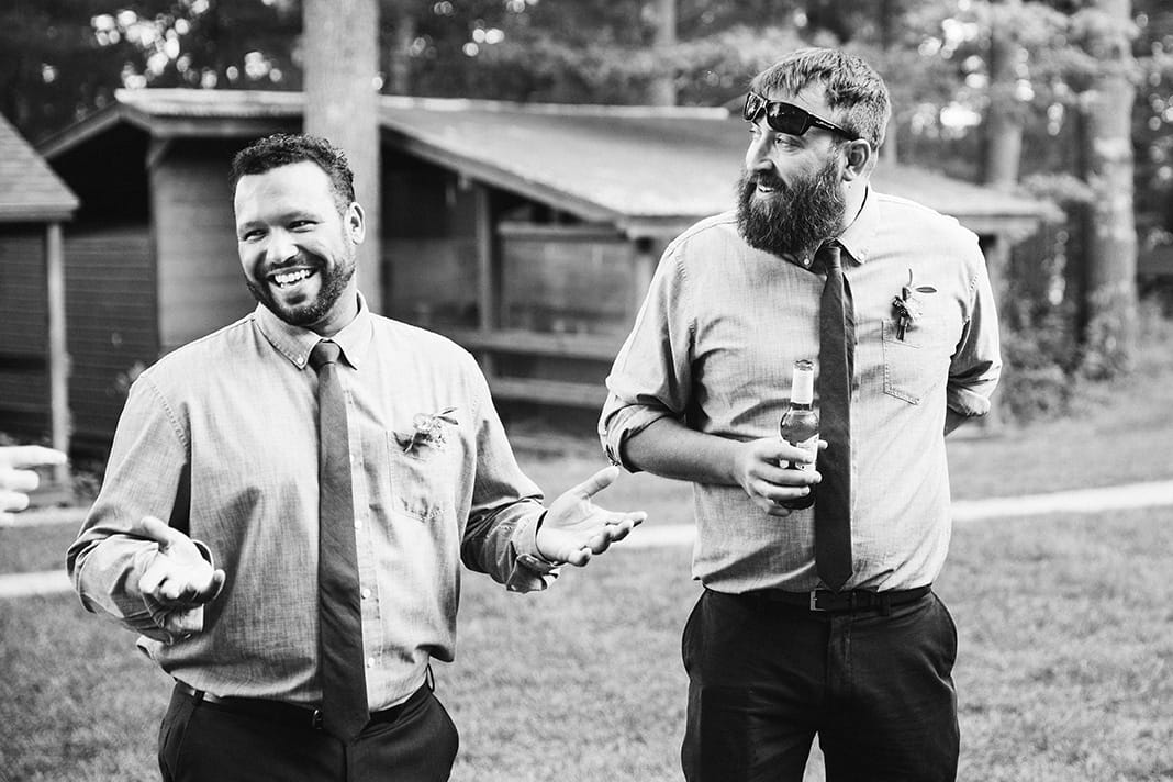 A documentary photograph of Groomsmen talking during cocktail hour at a Kingsley Pines Camp wedding in Maine