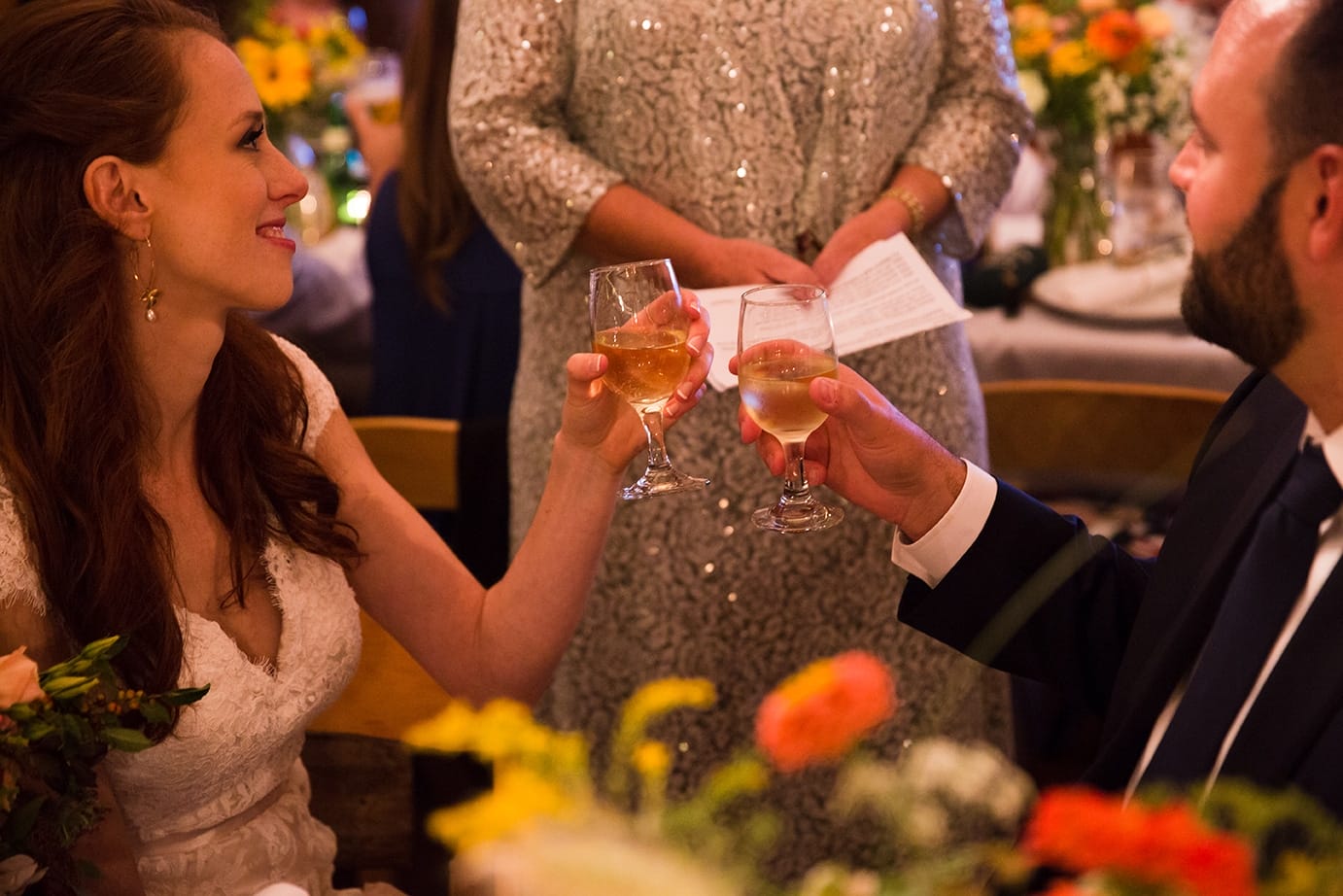 A documentary photograph of a bride and groom raising their glasses for a toast during their Kingsley Pines Camp wedding in Maine