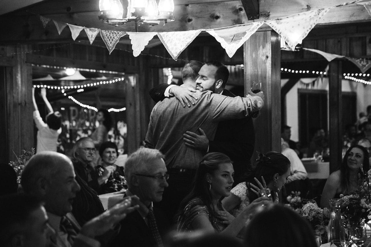 A documentary photograph of a groom hugging his best man during his Kingsley Pines Camp Wedding in Maine