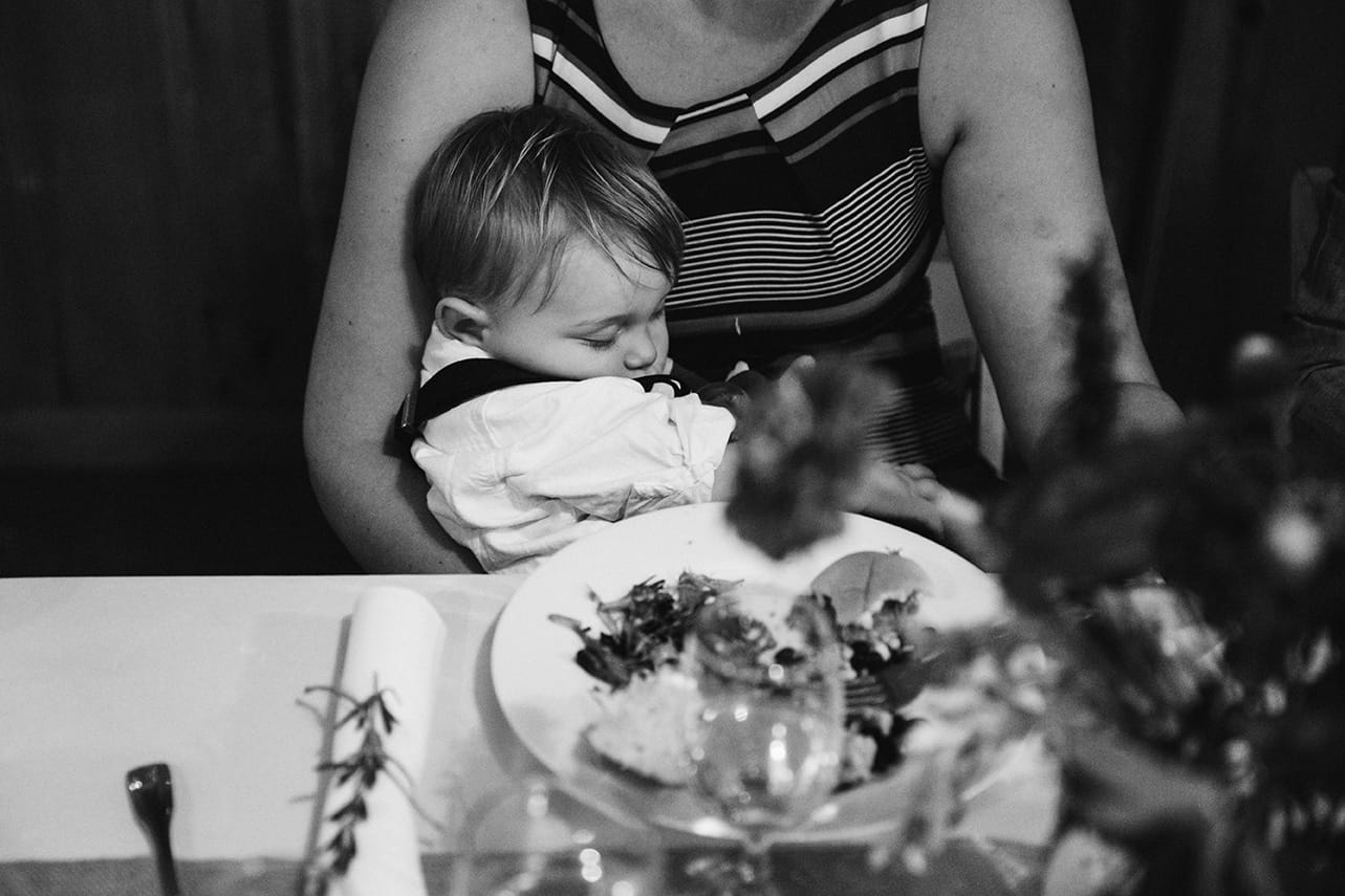 A documentary photograph of a baby sleeping in his mother's lap during a Kingsley Pines Camp Wedding in Maine