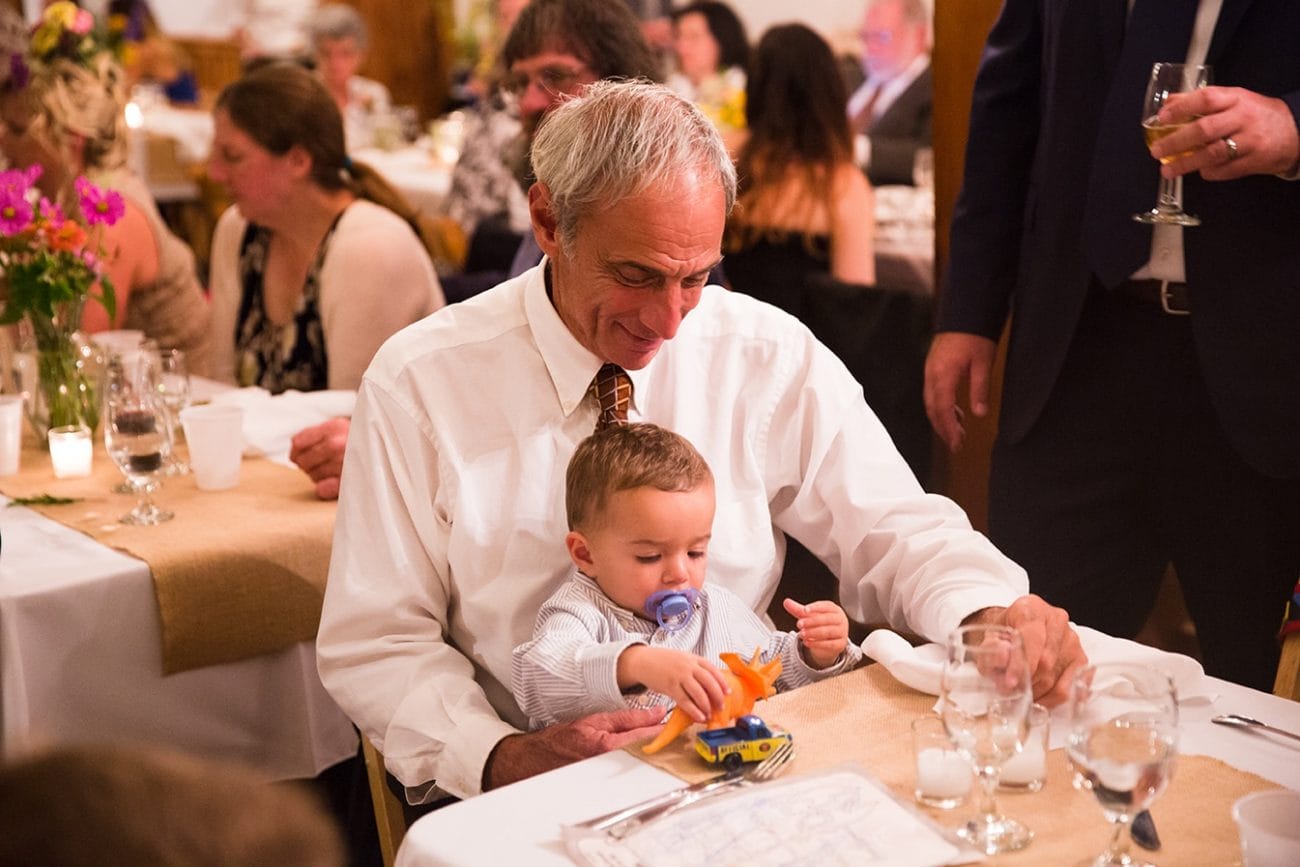 A documentary photograph of a grandfather playing with his grandson during a Kingsley Pines Camp Wedding in Maine