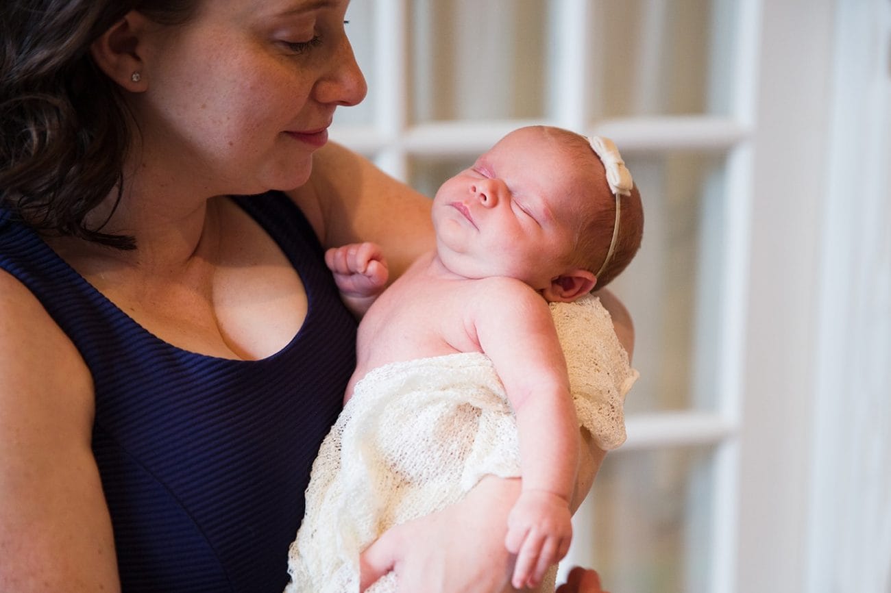 A lifestyle photograph of a mother with her baby girl during an in home newborn session in the Jamaica Plain neighborhood of Boston, Massachusetts