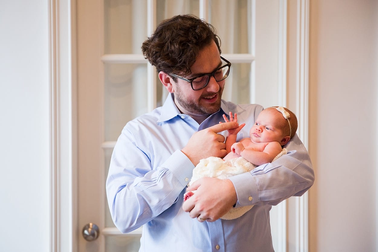 A lifestyle portrait of a father holding his baby girl during an in home newborn session in the Jamaica Plain neighbourhood of Boston, Massachusetts