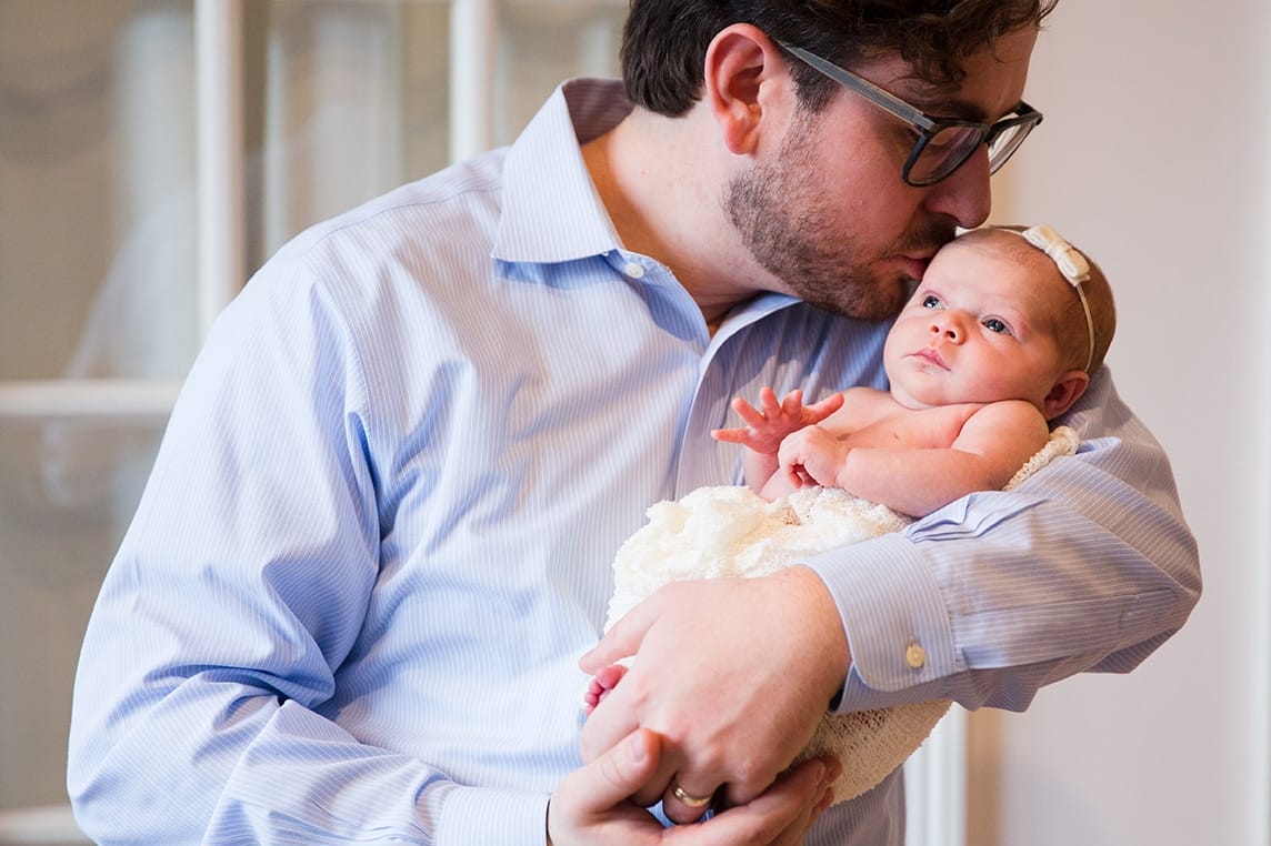 A lifestyle photograph of a father kissing his baby girl during an in home newborn session in the Jamaica Plain neighbourhood of Boston, Massachusetts