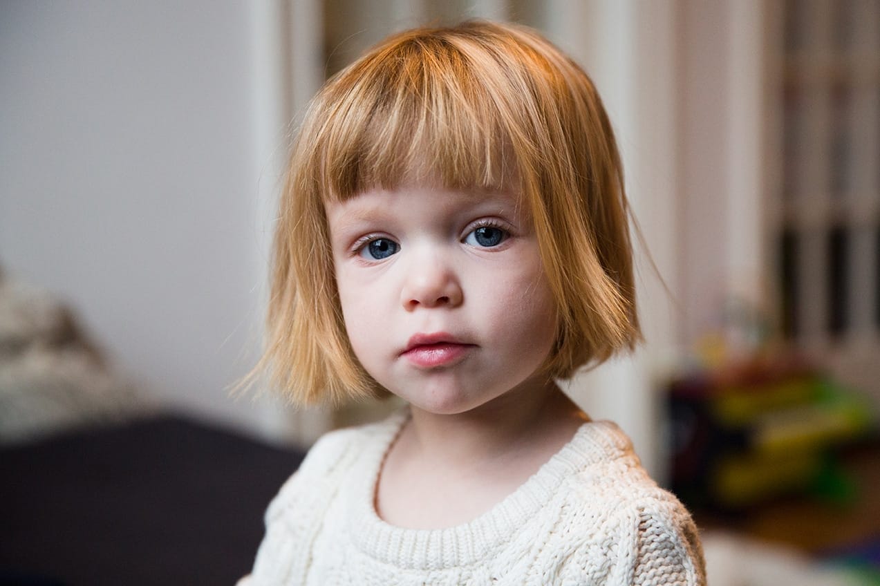 A portrait of a toddler during a her baby's sisters in home newborn session in the Jamaica Plain neighbourhood of Boston, Massachusetts