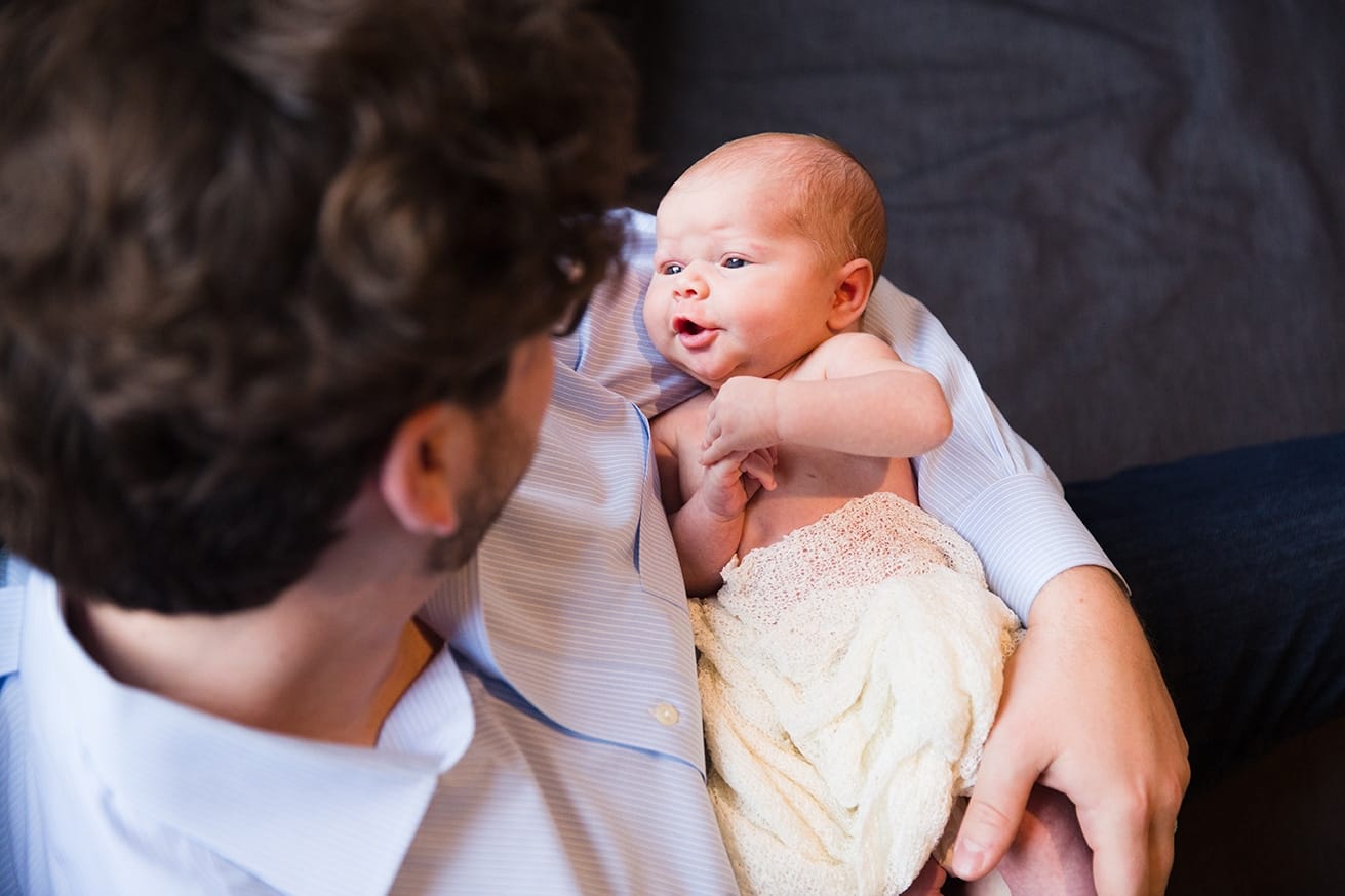 A lifestyle photograph of a father holding his new baby girl during an in home newborn session in the Jamaica Plain neighbourhood of Boston, Massachusetts