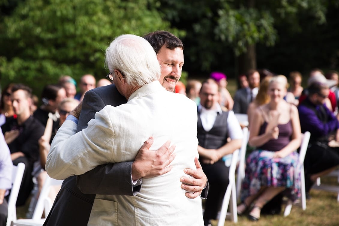 A documentary photograph of a Groom hugging his father at the top of the aisle during a Lyman Estate Wedding in Boston, Massachusetts