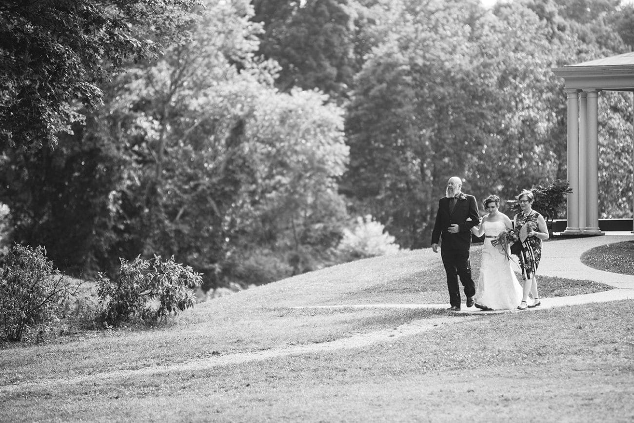 A documentary photograph of a bride walking down the aisle with her parents during a Lyman Estate Wedding in Boston, Massachusetts