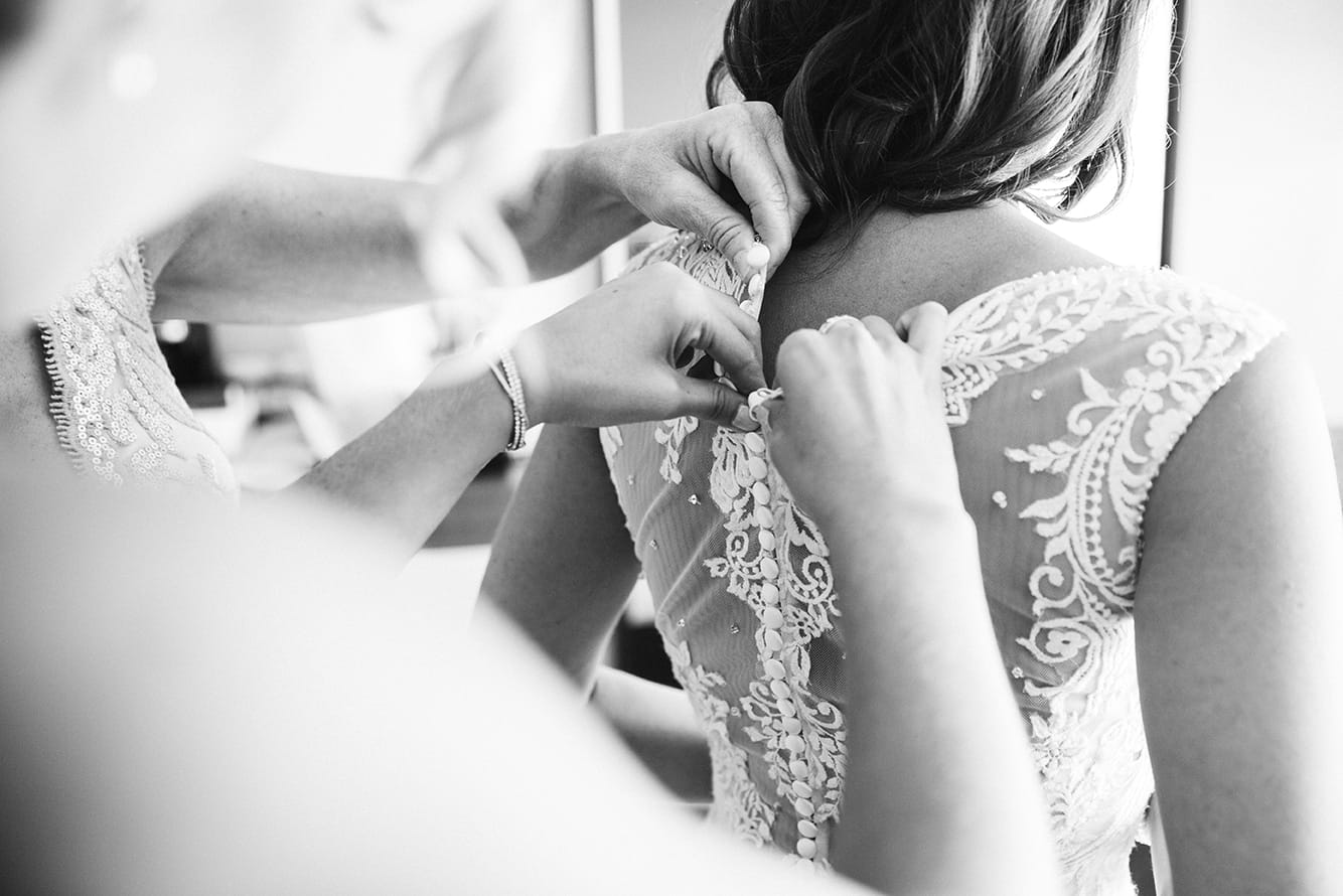 This documentary photograph of a mother and bridesmaid buttoning the brides dress is one of the best wedding photographs of 2016