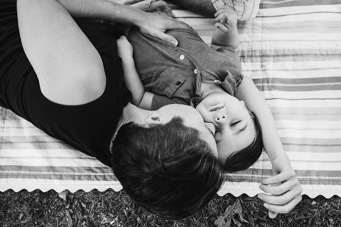 This lifestyle portrait of a mother kissing her son as they lay on a blanket in the park is one of the best family photographs of 2016