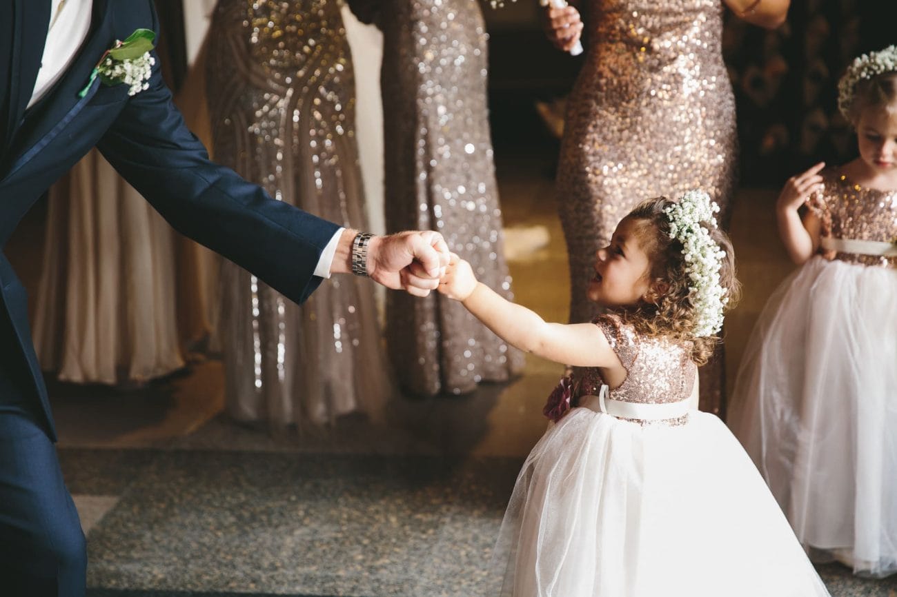 This documentary photograph of a flower girl fist bumping a groomsmen before the ceremony is one of the best wedding photographs of 2016
