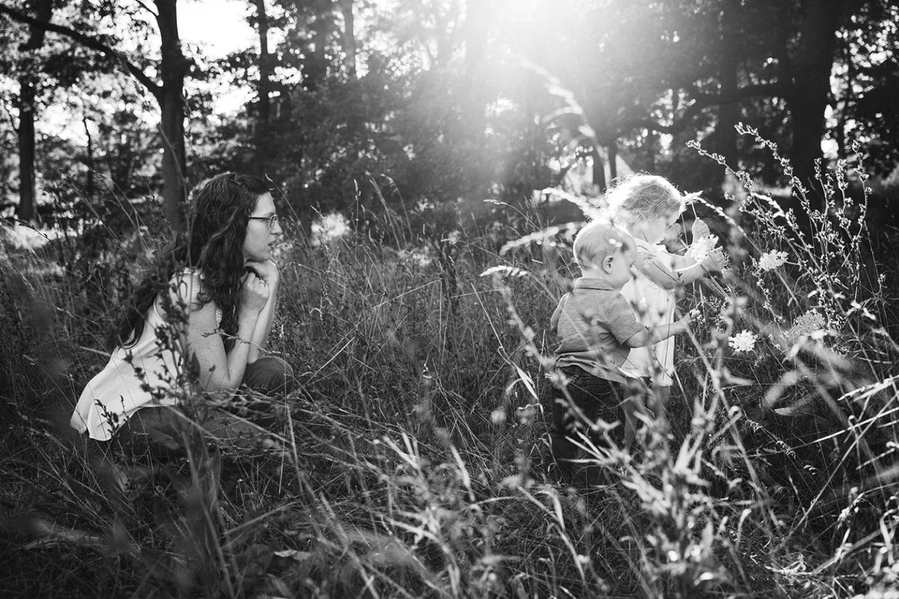 A documentary photograph of a mom walking her children pick flowers during an Arnold Arboretum Family Session in Boston, Massachusetts